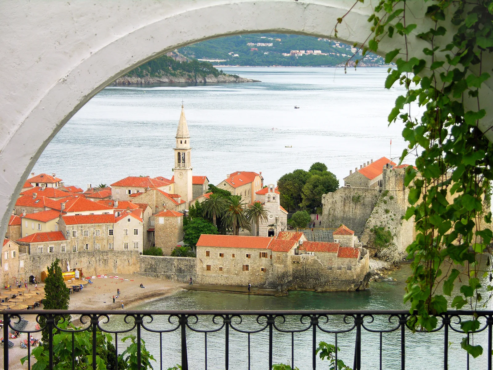 Budva Old Town and its church spire framed through a stone archway above the sea