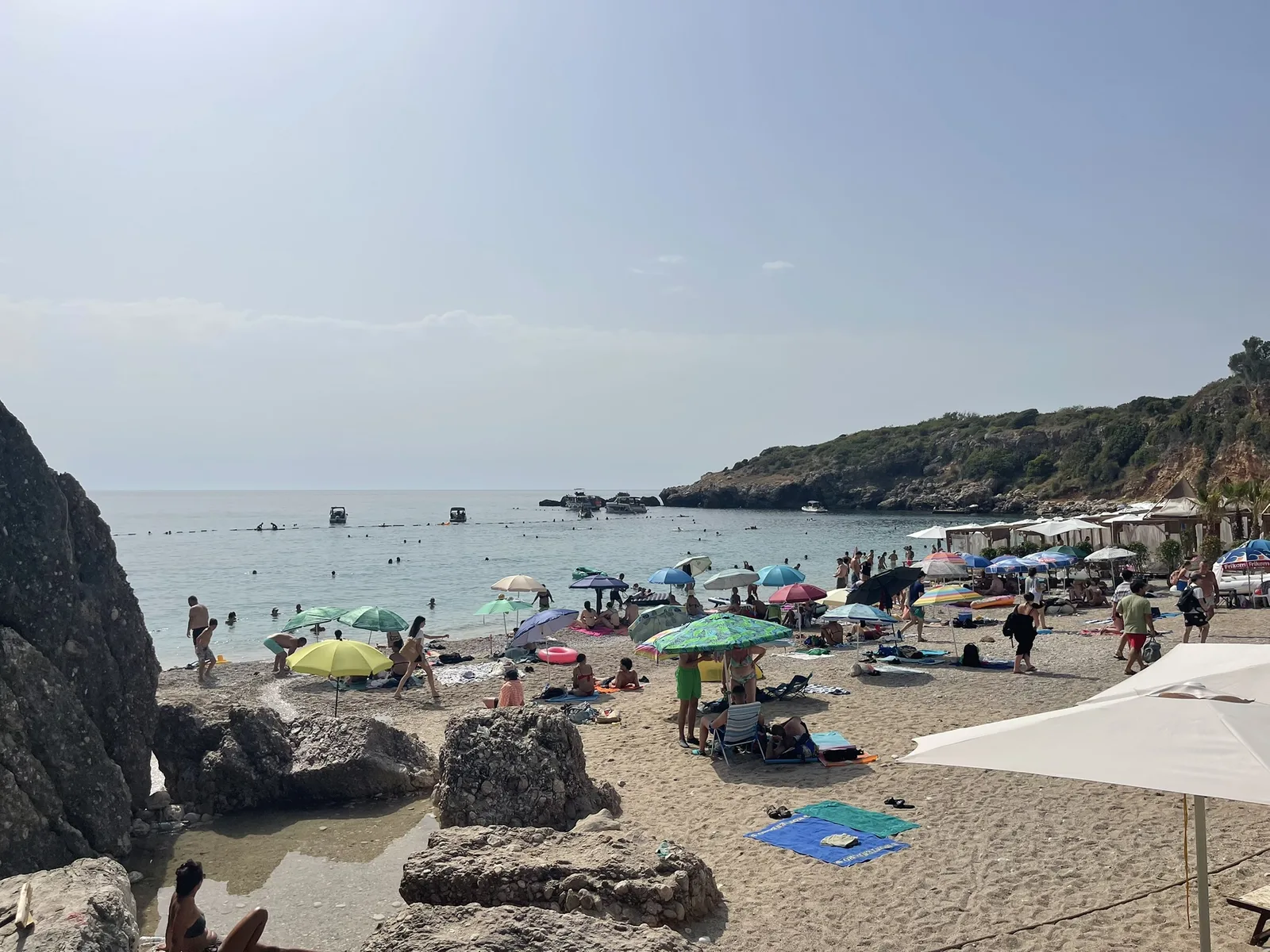 Rocks at the edge of Drobni Pijesak beach with bathers and parasols beyond