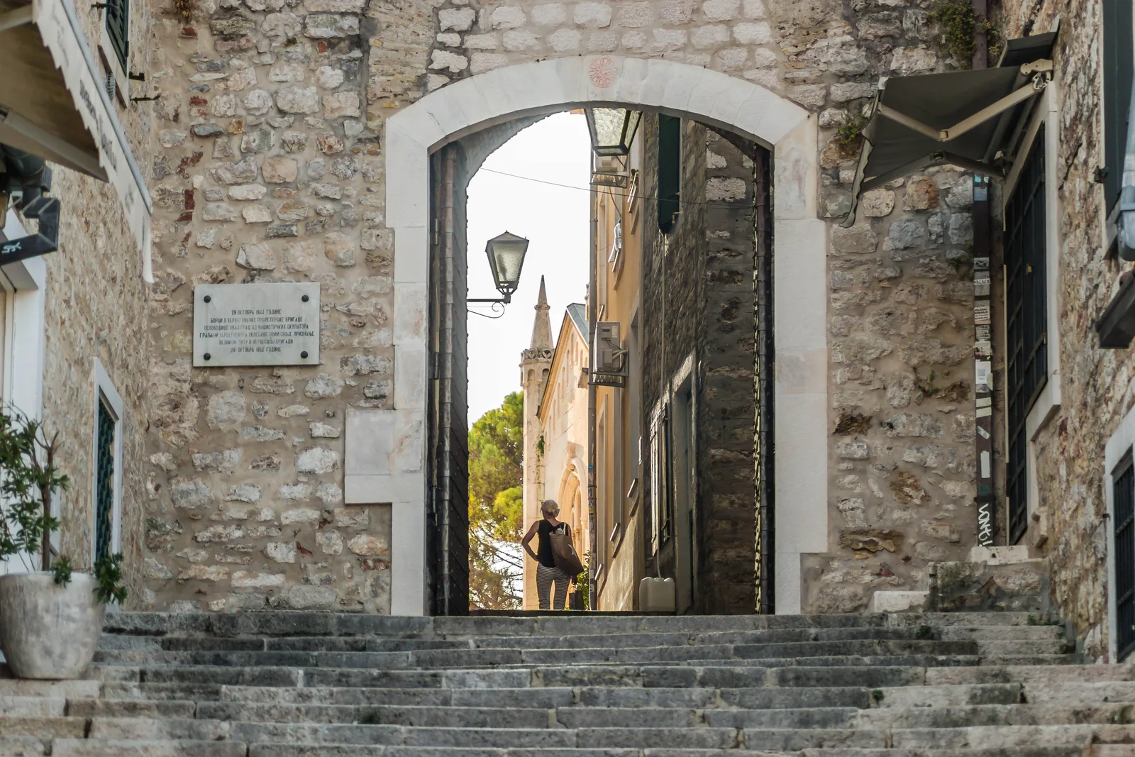 An arched Old Town gateway and stone steps in Herceg Novi, with a church spire beyond