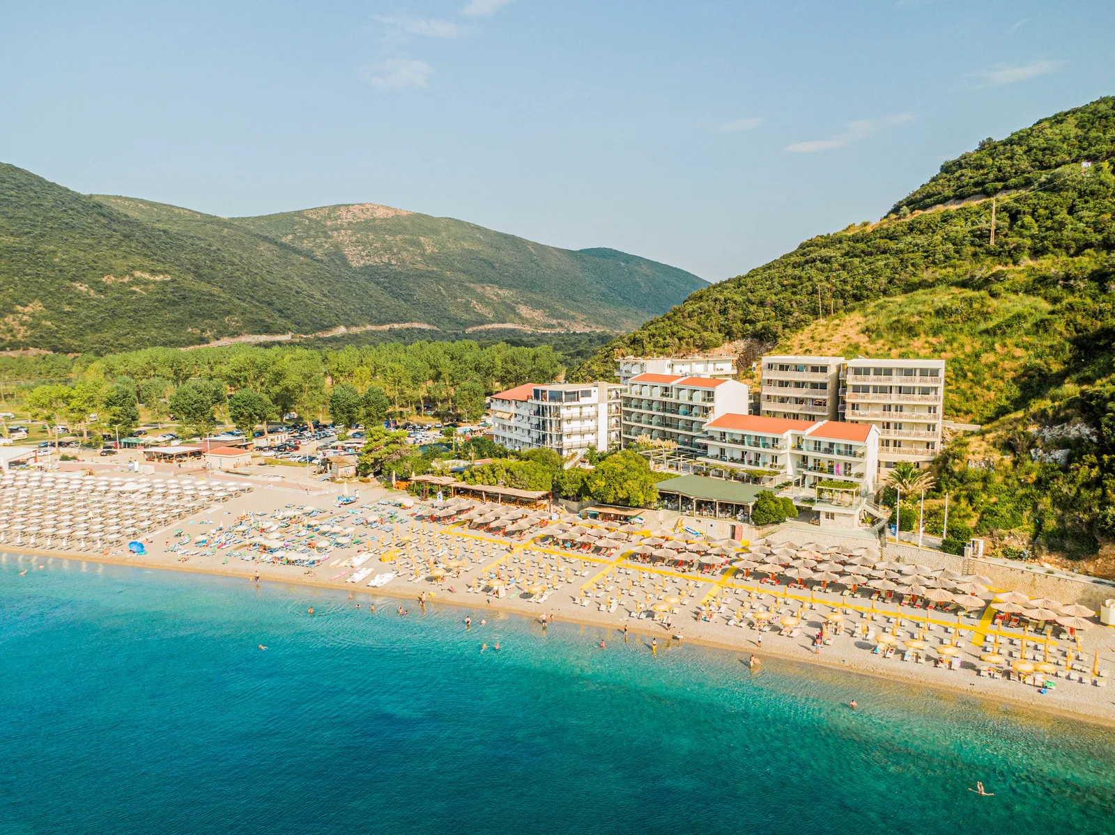 Jaz Beach resort end with hotels, umbrella rows and green mountains behind