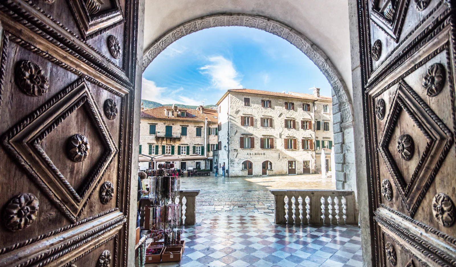 Vista de la plaza de la catedral de Kotor a través de una puerta de madera ornamentalmente tallada