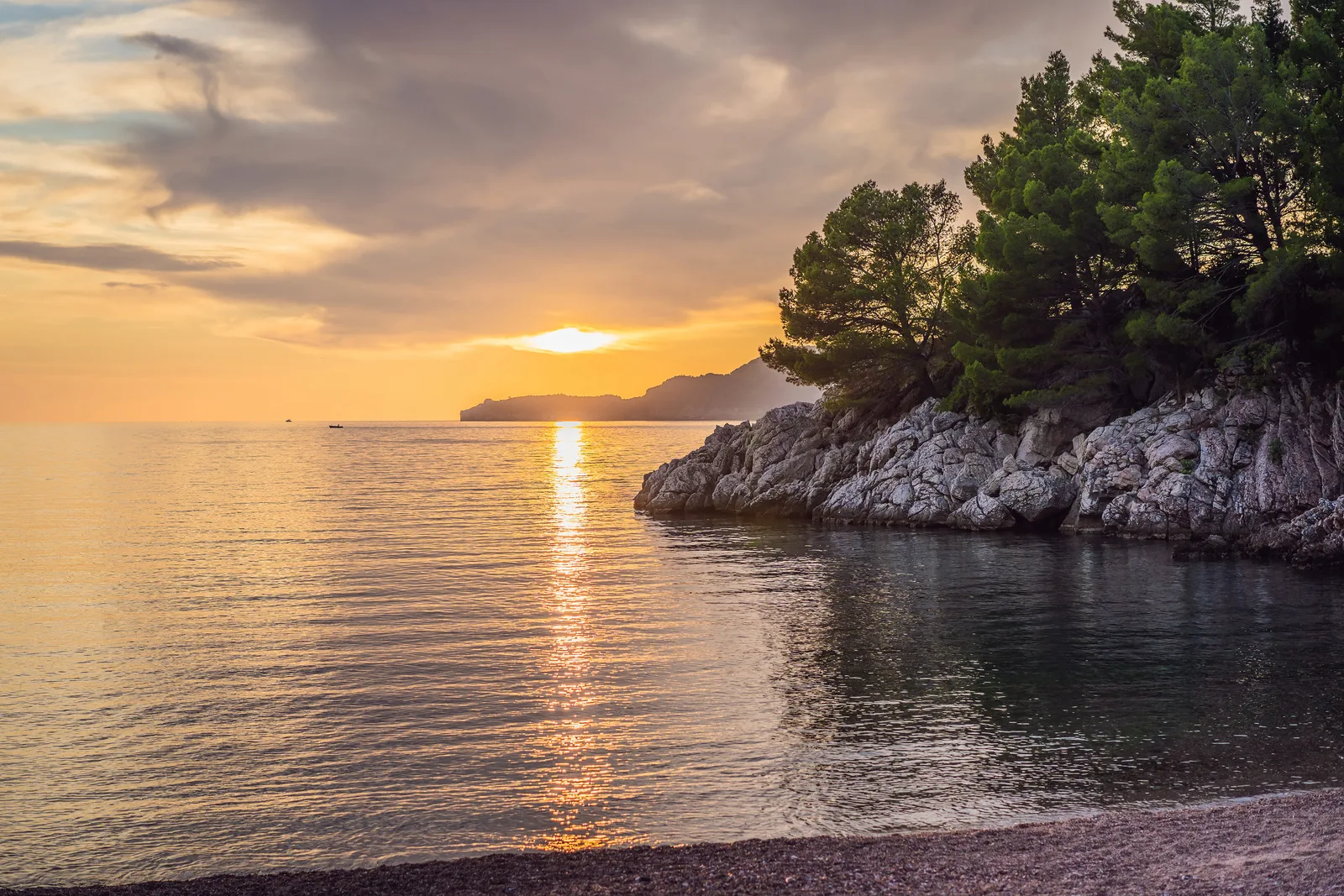 Sunset over the sea from a pine-fringed rocky cove at Milocer