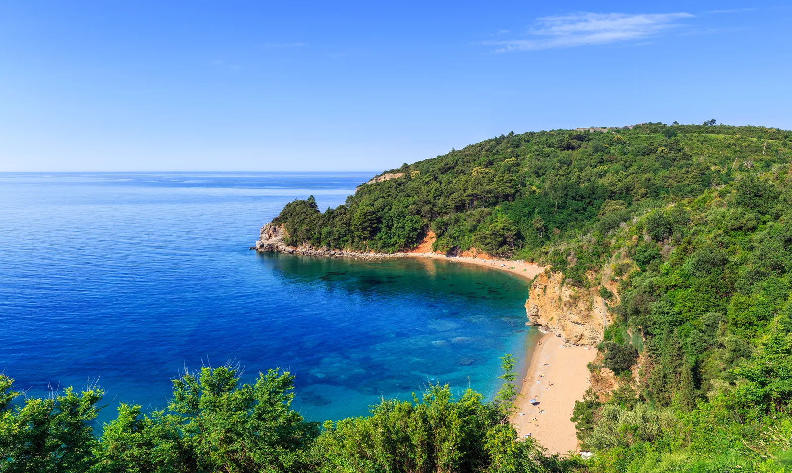 Una cala arenosa apartada enmarcada por colinas boscosas verdes en la costa cerca de Mogren Beach, Budva