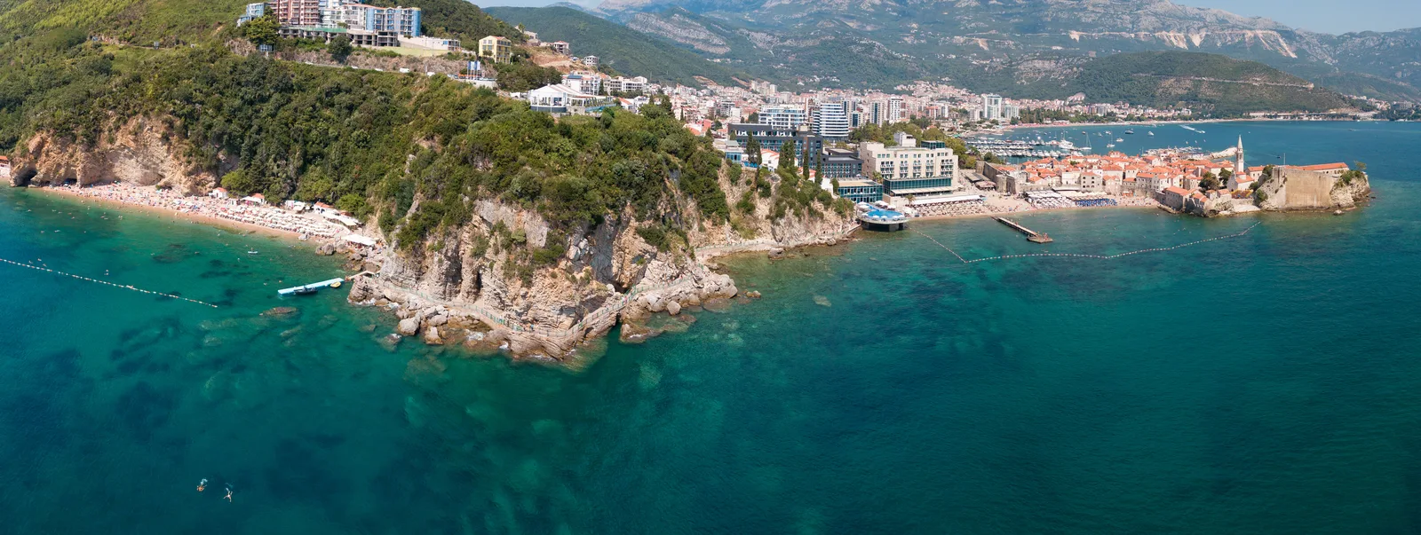 Mogren beach in Budva, a sandy cove tucked beneath steep rocky cliffs on the Adriatic.