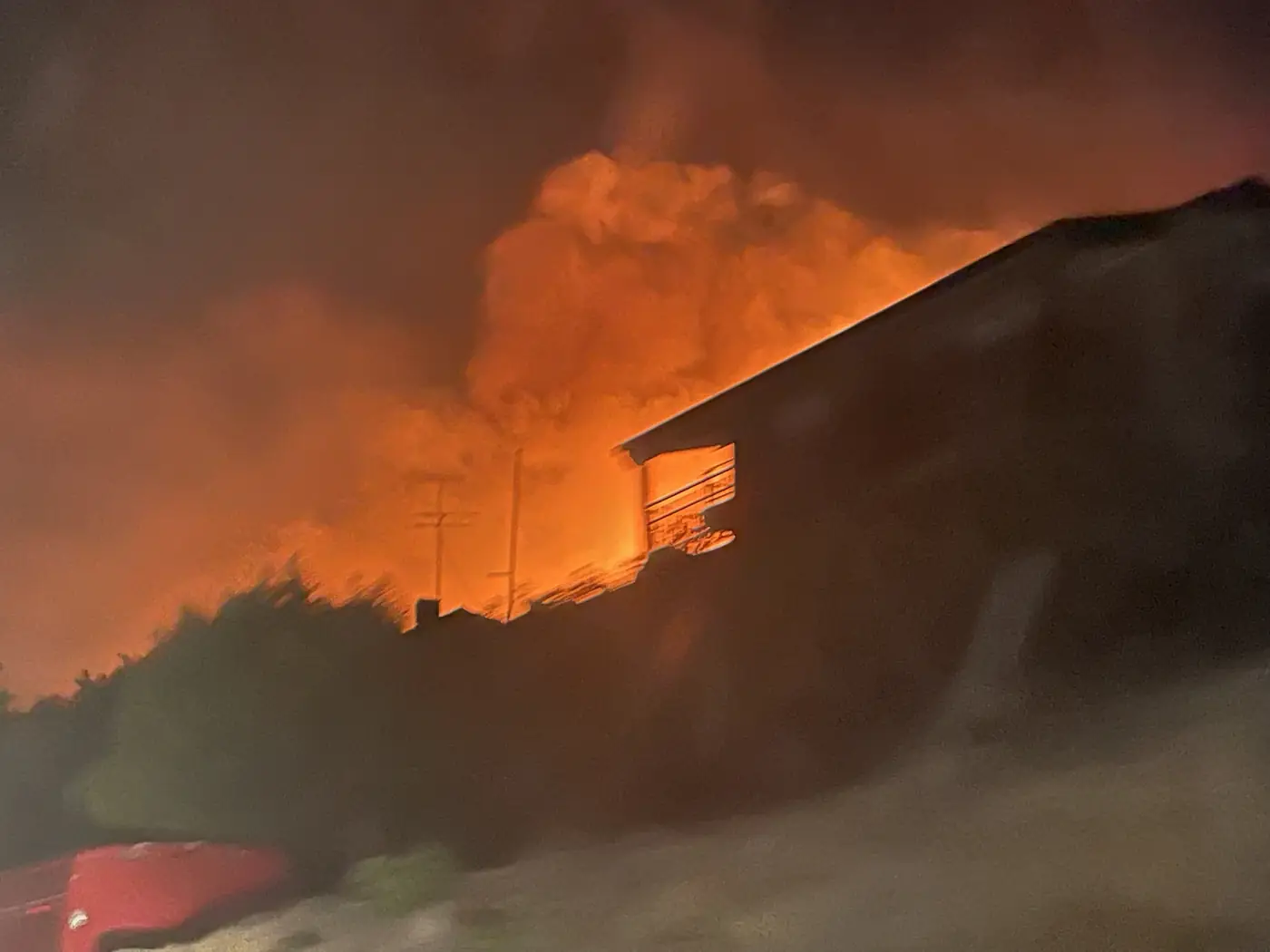 Flames rising directly behind the roofline of a building on the edge of Đenovići at night