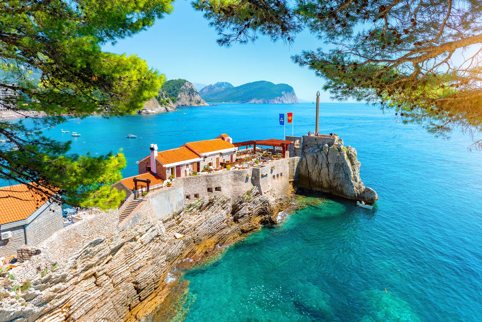 The Kastio fortress and its red-roofed Venetian building on the rocks at Petrovac, with turquoise water and pines