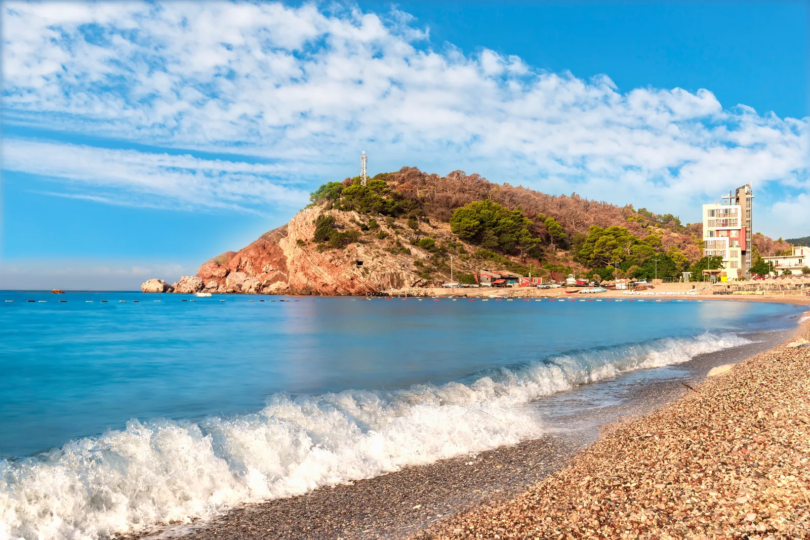Las olas rompiendo en la playa de guijarros de Sutomore debajo del promontorio de roca roja