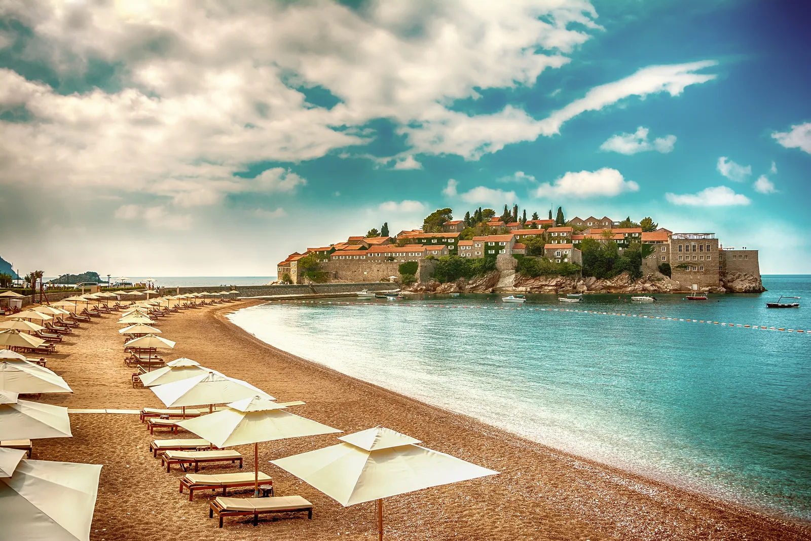 Sveti Stefan island and its pink-sand beach lined with umbrellas under a dramatic sky