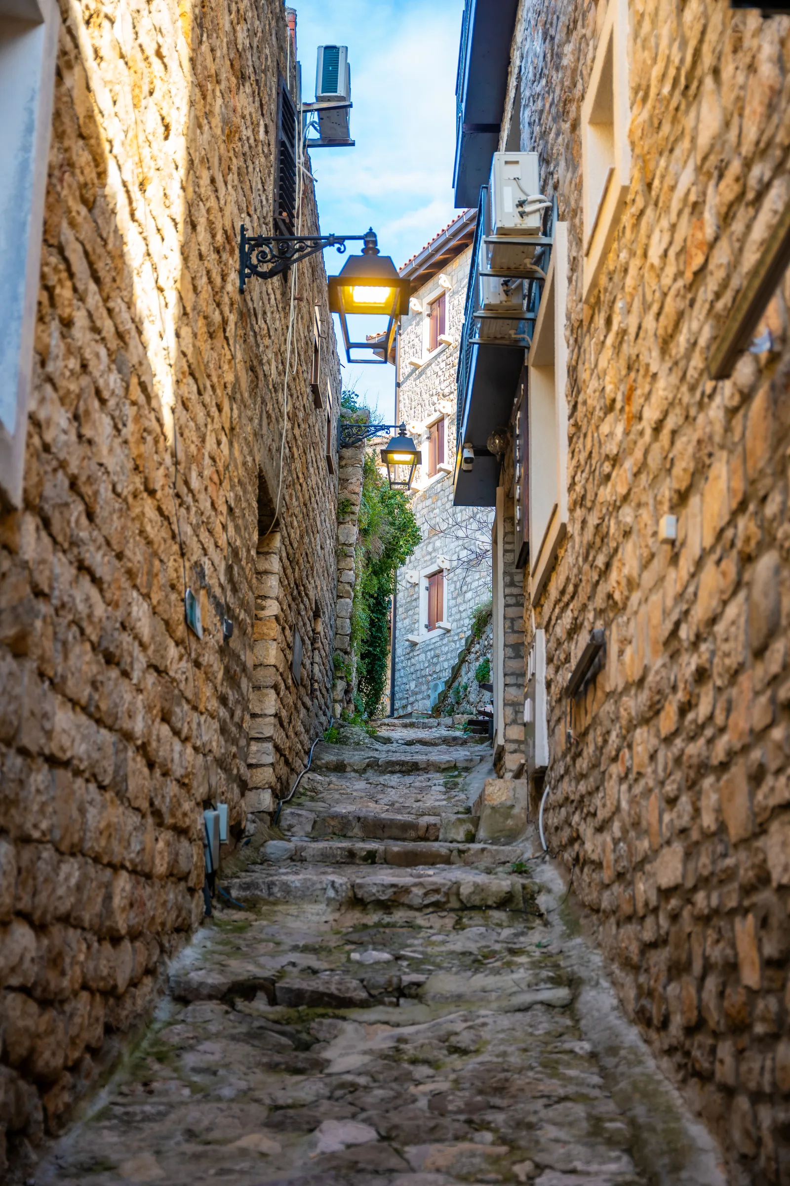 Un estrecho callejón empedrado y escalonado iluminado por faroles en el Casco Antiguo medieval de Ulcinj al atardecer