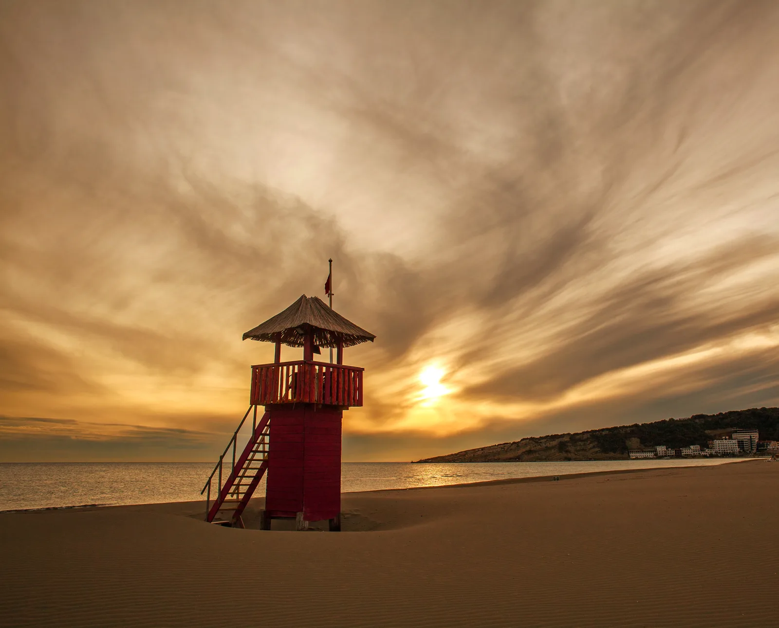 A red wooden lifeguard tower on the vast empty sands of Velika Plaza (Long Beach) near Ulcinj under a dramatic sky