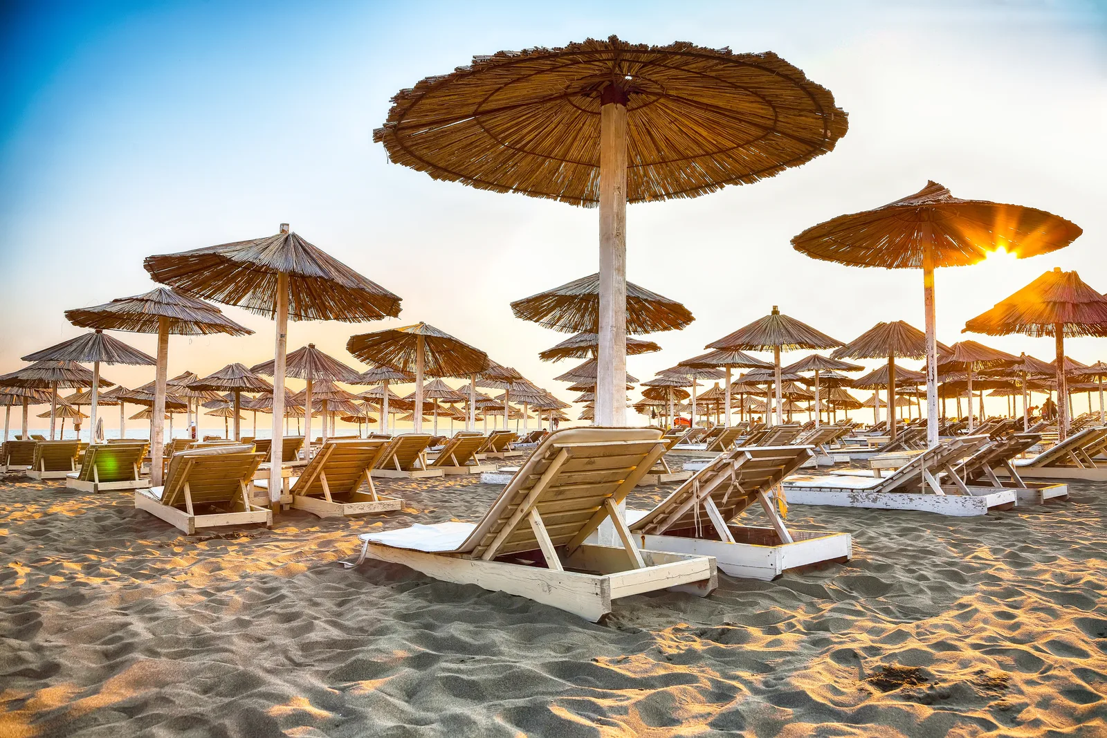 Rows of thatched straw umbrellas and wooden loungers at golden hour on Velika Plaza, Ulcinj
