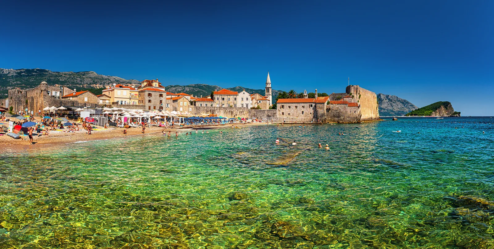 Ricardova Glava beach and swimmers in clear water below Budva's Old Town walls