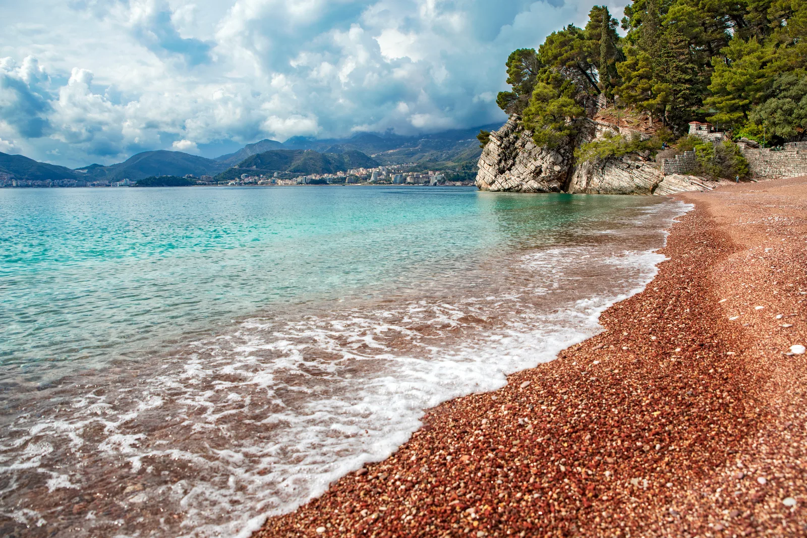 Quiet red-pebble beach on the Budva Riviera with turquoise water and mountains