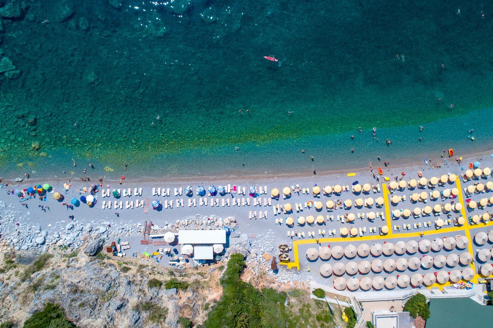 Aerial top-down of a Budva Riviera beach lined with sun umbrellas and loungers