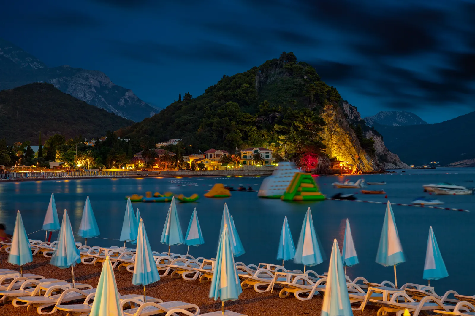 Petrovac beach at blue hour with rows of umbrellas and the lit headland behind