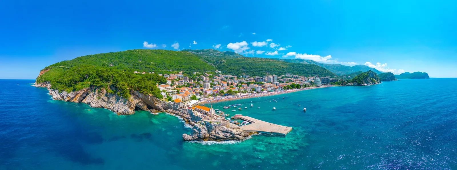 Aerial panorama of Petrovac, its peninsula, town and beach on the Budva Riviera