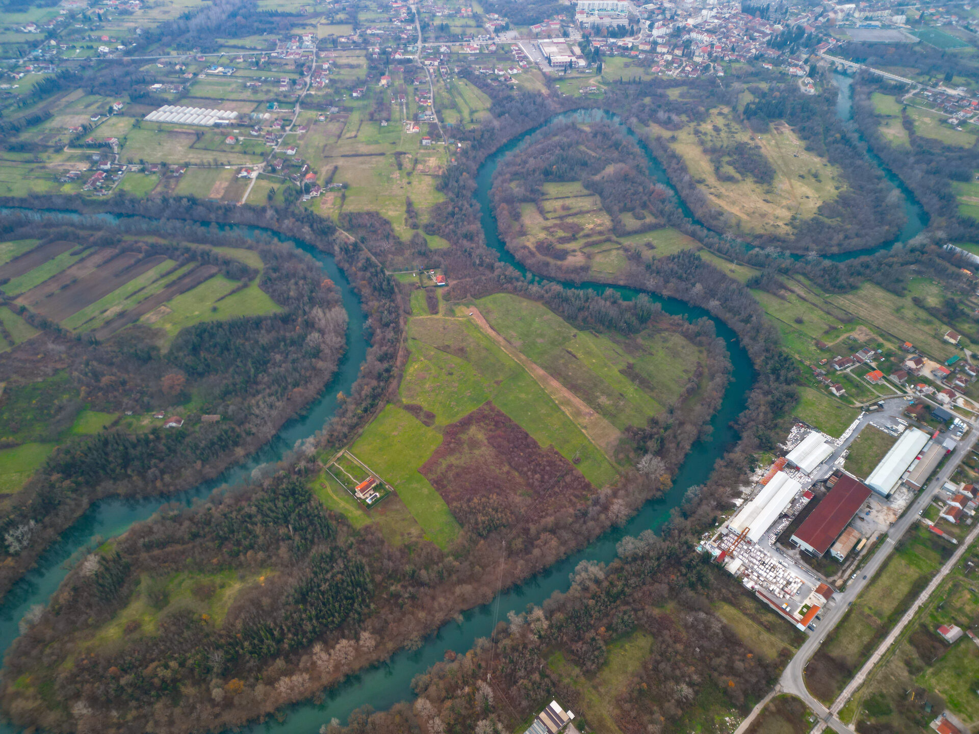 Aerial view of the clear Zeta river meandering in great curves through the green Bjelopavlici plain