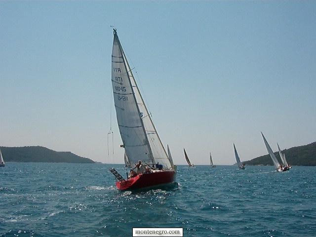 A yacht under sail heading out through the mouth of the Bay of Kotor towards the open Adriatic