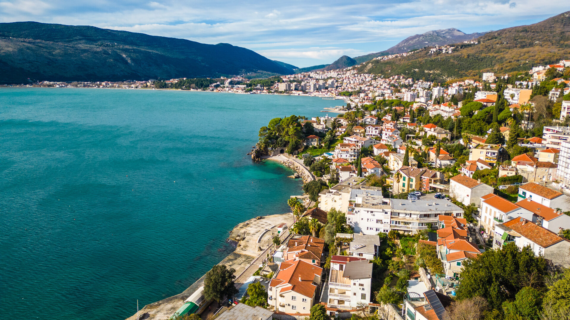 Red-roofed waterfront town along the Herceg Novi riviera with a turquoise bay and mountains behind
